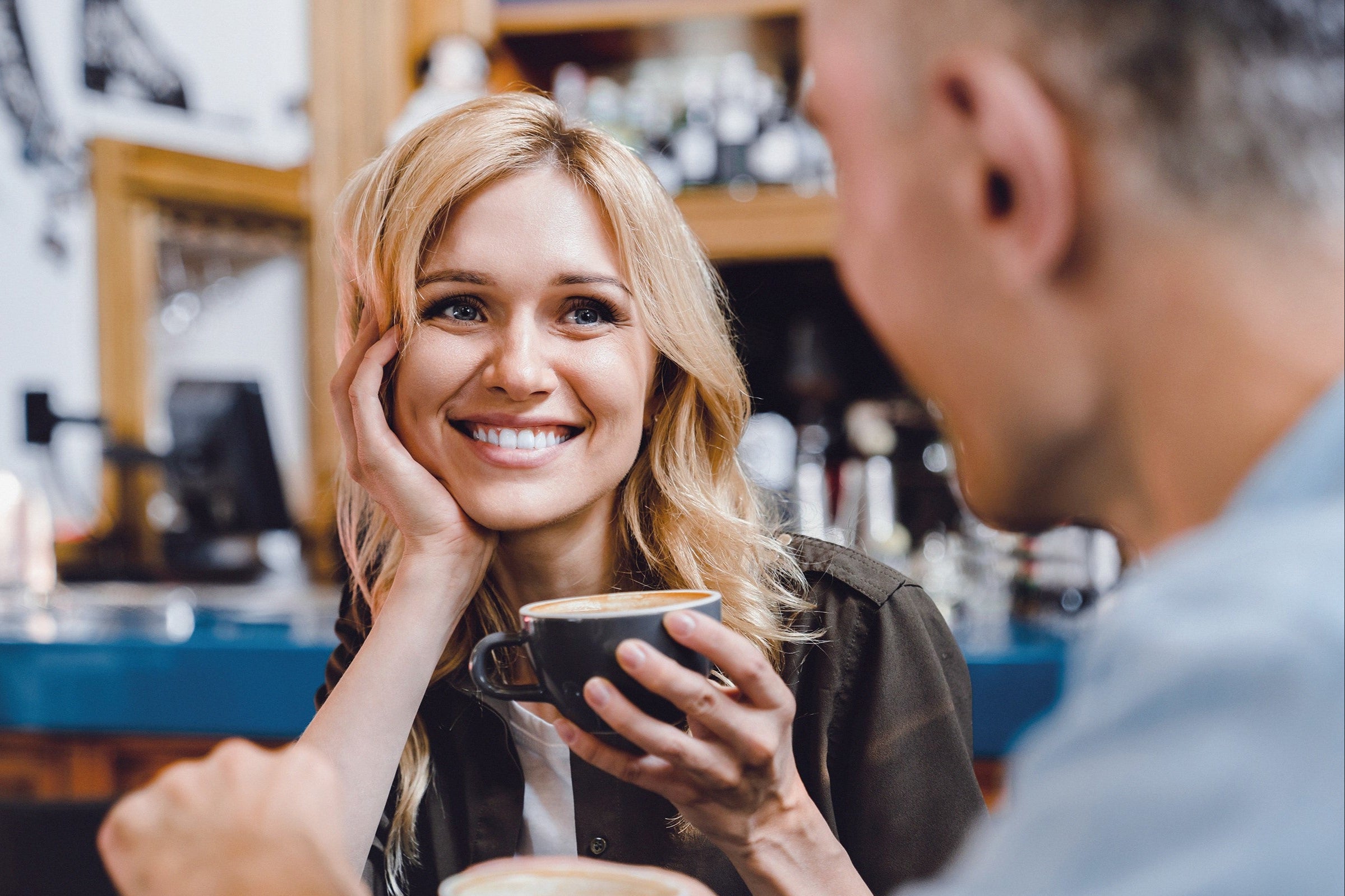 Frau in einem Café mit Cappuccino in der Hand lächelt gegenüber glücklich an.