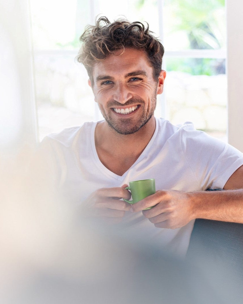 Mann sitzt auf einem Sessel und hält eine grüne Kaffeetasse