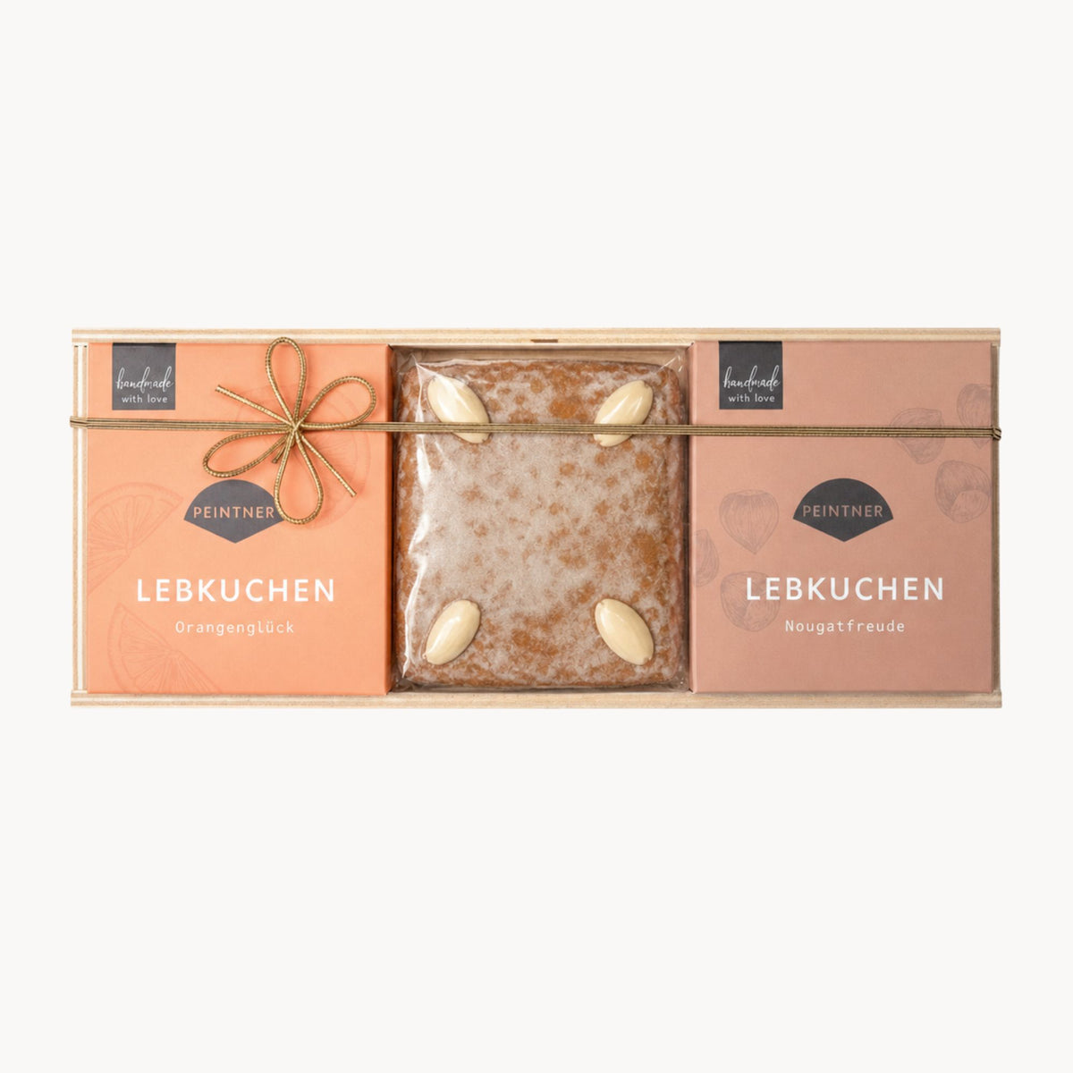 Lebkuchen-Set in einer Holzbox mit drei Teilen: links „Orangenglück“, in der Mitte ein Natur-Lebkuchen mit Mandeln, rechts „Nougatfreude“, alle Packungen mit Goldschleife.
