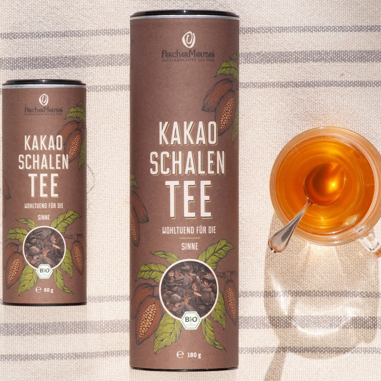 Kakaoschalentee 60g und 180g mit aufgebrühtem Tee in einer Glastasse mit Löffel daneben