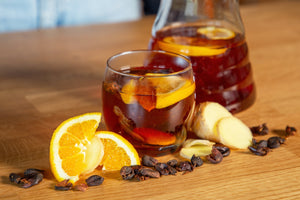 Alkoholfreier Cascara Punsch mit Orangenscheiben, Ingwer und Kaffeekirschen – serviert im Glas und in einer Karaffe auf Holztisch