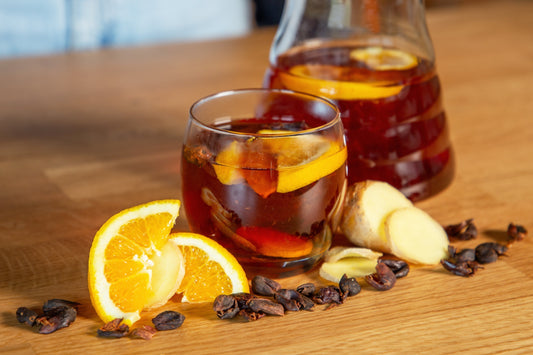 Alkoholfreier Cascara Punsch mit Orangenscheiben, Ingwer und Kaffeekirschen – serviert im Glas und in einer Karaffe auf Holztisch