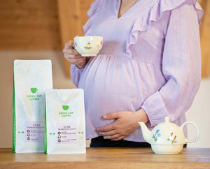 Schwangere Frau mit entkoffeiniertem Kaffe in der Hand und zwei Decaf-Kaffee Luna Tüten (250g und 1kg) im Vordergrund