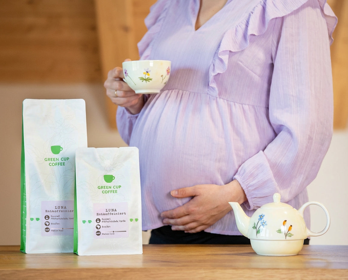 Schwangere Frau mit entkoffeiniertem Kaffe in der Hand und zwei Decaf-Kaffee Luna Tüten (250g und 1kg) im Vordergrund