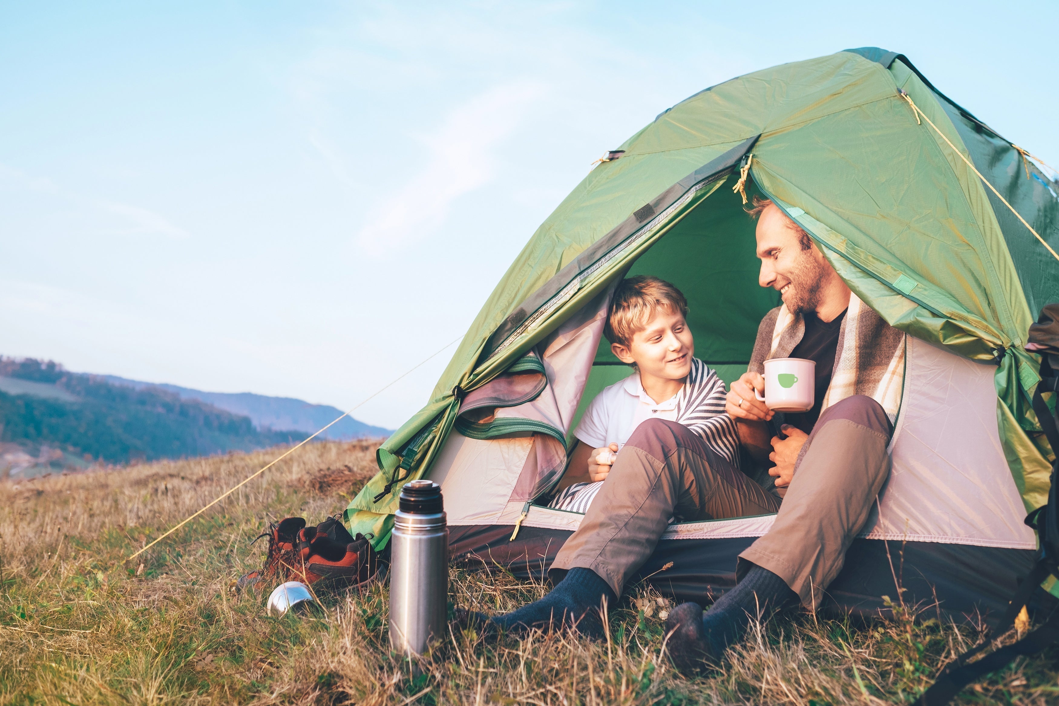 Outdoor Kaffee: Vater und Sohn sitzen im zelt, vater trintk eine tasse kaffee