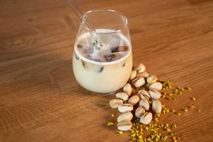 Pistazien Spanish Latte im Glas mit Glasstrohhalm auf Holztisch mit Pistazien