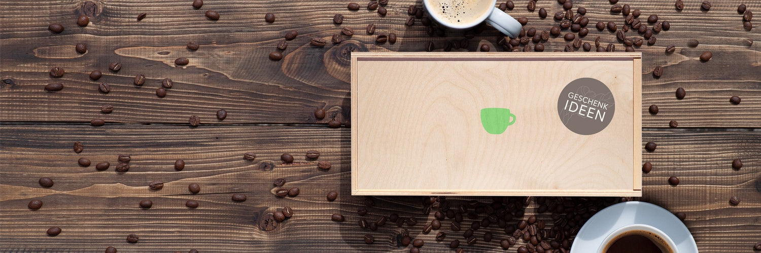 Geschenkbox mit Green Cup Coffee Logo auf Holztisch, umgeben von Kaffeebohnen und zwei Tassen Kaffee – kreative Kaffeeideen stilvoll verpackt