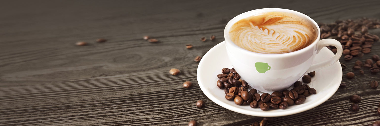 Tasse Cappuccino mit Latte Art auf Untertasse, umgeben von Kaffeebohnen auf Holzuntergrund – Symbol für hochwertigen Kaffeegenuss