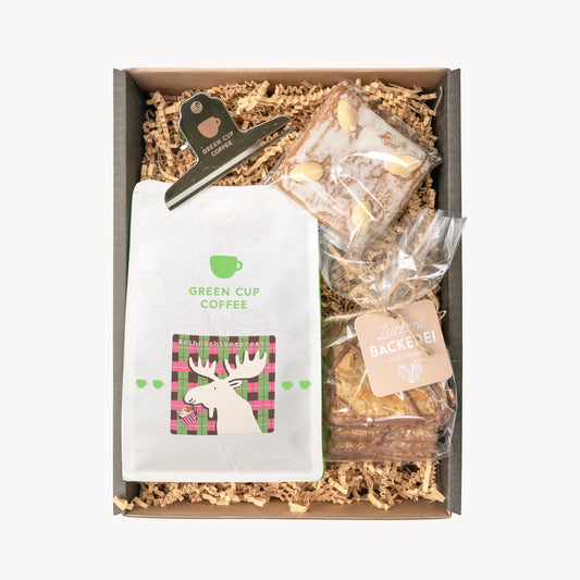 Geschenkbox mit einer Tüte Weihnachtsespresso, Mandelplättchen mit Schokoladenstreifen, einem Lebkuchen in Natur mit Mandeln und einem silbernen Kaffeetütenclip mit Green Cup Coffee Logo.