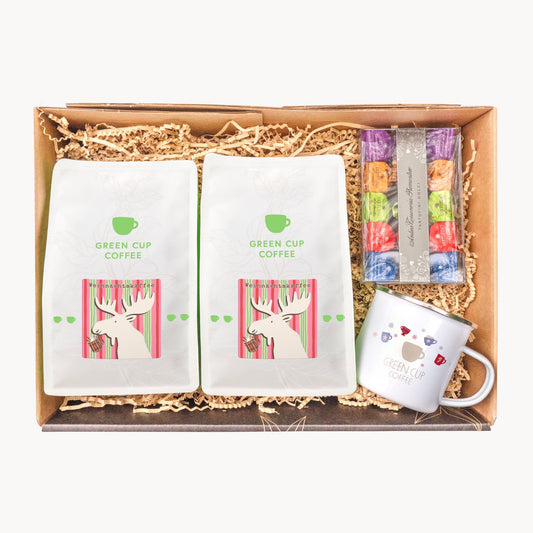 Geschenkkarton mit zwei Tüten Weihnachtskaffee, einer Packung Tartufo Dolce und einer weißen Emailletasse mit Green Cup Coffee Logo.